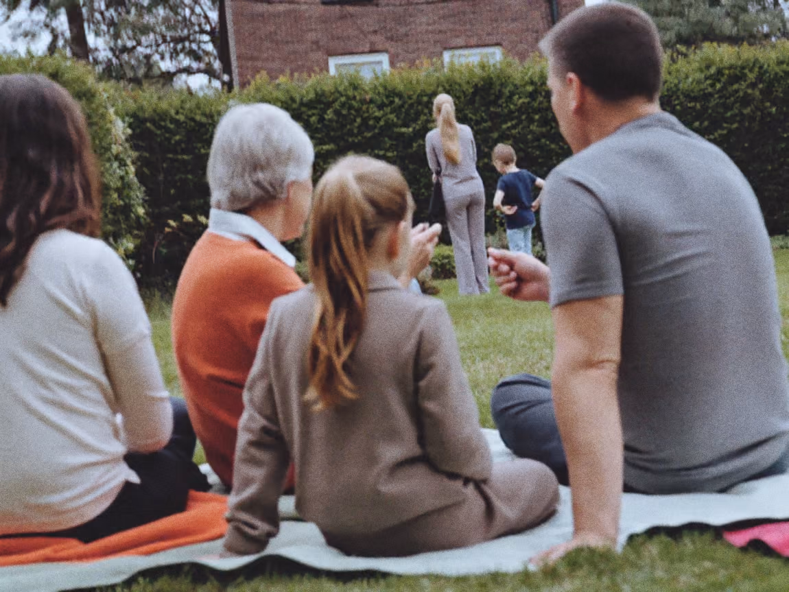 Familie kijkt vanaf picknickkleden toe in de tuin tijdens een familiedag